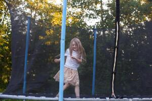 poco bambino ragazza salto su il trampolino nel il indietro cortile foto