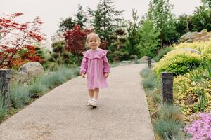 poco bambino ragazza nel elegante vestito a piedi nel estate giardino foto