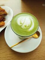 un' tazza di verde tè latte macchiato con un' bianca tazza e oro cucchiaio foto