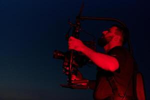 ore notturne catturare. professionale operatore video film atleti in esecuzione nel illuminato di rosso buio foto