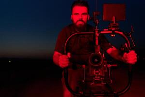 ore notturne catturare. professionale operatore video film atleti in esecuzione nel illuminato di rosso buio foto