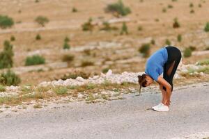 determinato femmina atleta allungamento dopo un intenso correre attraverso aspro montagna terreno. foto