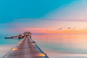 tramonto sull'isola delle maldive, resort di ville sull'acqua di lusso e molo in legno. bel cielo e nuvole e sfondo della spiaggia per le vacanze estive e il concetto di viaggio. paesaggio al tramonto paradisiaco foto