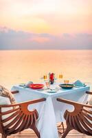 romantico cena su il spiaggia con tramonto, candele con elegante tavolo, tramonto cielo e mare. sorprendente luna di miele e anniversario coppia destinazione. romanza e amore sfondo foto