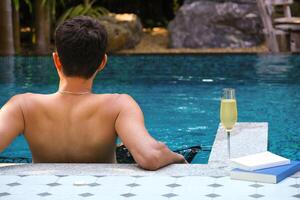 un' uomo rilassante nel un' nuoto piscina con un' bicchiere di Champagne e libro a un' lusso ricorrere. vacanza, viaggiatore, rilassare tempo concetto. tropicale esotico vacanze vacanza, turismo e viaggio. foto