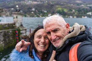 contento mezzo anziano coppia su vacanza assunzione un' autoscatto su il sponde di lago maggiore foto