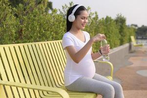 bellissimo incinta donna potabile bottiglia di puro acqua nel il parco, salutare e attivo gravidanza stile di vita concetto. foto