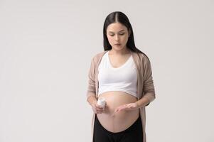 ritratto di bellissimo incinta donna assunzione pillola e vitamina al di sopra di bianca sfondo studio, Salute e maternità concetto foto