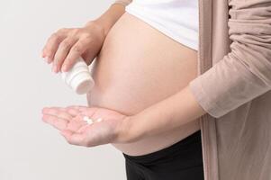 ritratto di bellissimo incinta donna assunzione pillola e vitamina al di sopra di bianca sfondo studio, Salute e maternità concetto foto