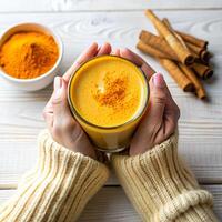 mani Tenere bicchiere di biologico curcumina miele d'oro latte, indiano Curcuma latte macchiato su bianca di legno tavolo sfondo. superiore Visualizza spezie giallo chai naturale bevanda salutare cibo concetto foto