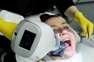 ultimo tecnologia nel dentale clinica nuovo raggi X scanner donna è prese immagine dopo Riempimento canali donna sorrisi bella medico giallo guanti speciale dispositivo per fotografia fauci di denti e gengive raggi X foto