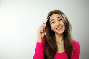 graffiare il tuo capelli con un' penna giovane donna ragazza giocando penna nel mano in linea apprendimento riluttanza per imparare alunno vita Scrivi dettatura disegno matita ragazza nel un' rosa maglione su un' bianca sfondo studio foto