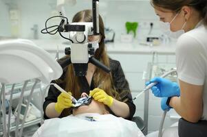 dentale più recente ufficio nuovo attrezzatura protesi canali otturazioni moderno dentale attrezzatura medio tiro di femmina dentista nel nero cappotto, maschera e guanti utilizzando dentale microscopio per esaminare pazienti denti foto