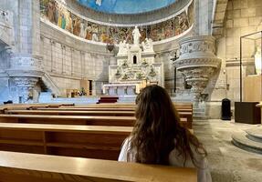 un' ragazza con lungo capelli nel un' vestito si siede dentro il Chiesa e sembra a il iconostasi diocesano santuario viana fare castello, nel Portogallo foto