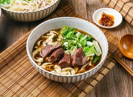 classico Manzo guancia tagliatelle con peperoncino salsa, primavera cipolla, di legno cucchiaio, e bastoncini servito nel piatto isolato su stuoia lato Visualizza di taiwanese cibo foto