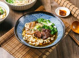 glutine Manzo tagliatelle con peperoncino salsa, primavera cipolla, di legno cucchiaio, e bastoncini servito nel piatto isolato su stuoia lato Visualizza di taiwanese cibo foto