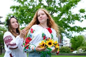 ragazza siamo seduta nel parco in attesa per vacanza per tessere capelli treccia treccia ghirlande di fiori su testa Aiuto amico tenerezza bellezza giovane parrucchiere giovane donne siamo preparazione per celebrazione foto