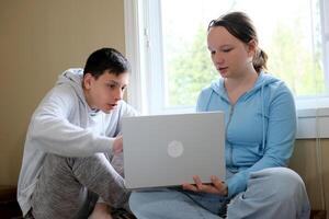 spiegare lezione ragazzo mostrando ragazza su computer porzione studia amici più vecchio fratello minore sorella in linea apprendimento la spesa tempo insieme seduta di il finestra con un' il computer portatile nel mani adolescenti foto