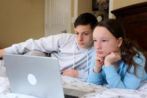 felicissimo bambini sorella fratello ridendo trascorrere fine settimana gratuito tempo insieme a casa su divano letto mangiare Popcorn. adolescente bambini Guardando cartone animato uso a distanza controllo su il computer portatile avere divertimento. film notte foto