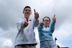 ragazzi ragazza pollici su approvazione piace mostrando classe essere contento ridendo contro il cielo all'aperto adolescenti avendo divertimento freddo tempo metereologico cielo con nuvole un' lotto di gioia felicità relazioni nel adolescenza divertimento foto