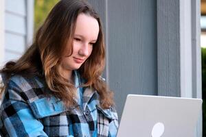 adolescenziale ragazza con un' il computer portatile seduta su il veranda di il Casa. lei Guardando il notizia fare compiti a casa in linea conferenza zaino cartella acqua bottiglia matita ordinario persone vero vita foto