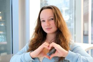 fabbricazione un' cuore con mani confessione scelta bellissimo adolescente ragazza in piedi di il finestra Tenere sua mani a il petto livello pieghevole un' positivo cartello pace nel Ucraina amore sentimenti Salute pubblicità foto