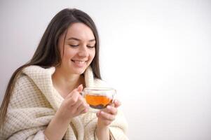 contento giovane donna potabile un' tazza di tè nel un autunno mattina. sognare ragazza seduta nel vivente camera con tazza di caldo caffè godendo sotto coperta con chiuso occhi. bella donna indossare maglione a casa. foto