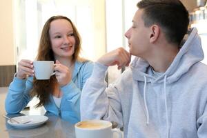 un' ragazzo e un' ragazza adolescenti su il primo vedendo ogni altro potabile caffè nel un' luminosa bar conversazione comunicazione Sorridi piace ogni altro Guarda a ogni altro leggero gli sport Abiti primo amore foto