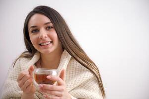 contento biondo donna con mazzo acconciatura riscaldamento e copertina a maglia plaid godendo nel sua caffè tempo di il finestra nel freddo inverno giorno. pace di mente e mentale Salute. foto