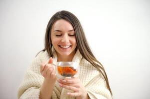 contento giovane donna potabile un' tazza di tè nel un autunno mattina. sognare ragazza seduta nel vivente camera con tazza di caldo caffè godendo sotto coperta con chiuso occhi. bella donna indossare maglione a casa. foto