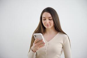 contento ritratto bellissimo carino giovane donna sorridente emozionato, adolescente ragazza digitando testo Messaggio su inteligente mobile Telefono gode in linea comunicazione isolato, studio tiro su bianca sfondo con copia spazio foto