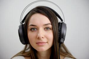 avvicinamento viso di ragazza nel cuffie su bianca sfondo studio vicino il computer portatile lento movimento vicino Guarda bellissimo giovane viso carino donna libero professionista opera come musicista sociale Aiuto comunicazione su Internet foto