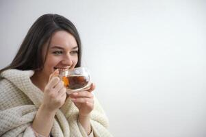 ritratto di malato moderno 20 anni vecchio casalinga nel rotolo collo maglione e cardigan mostrando tazza di caldo tè con Zenzero, Limone e miele isolato su inverno leggero blu sfondo. foto