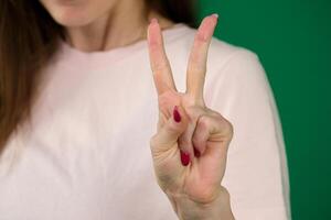 femmina mano con manicure mostrando Due dita tiro avvicinamento corpo parti di un' giovane donna su un' verde sfondo chiave cromatica foto