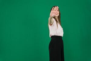 ritratto di un' grave giovane donna in piedi con disteso mano mostrando fermare gesto isolato al di sopra di verde sfondo foto