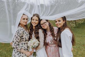 quattro ragazze siamo avendo divertimento nel natura sotto il della sposa velo. il sposa circondato di sua amici foto