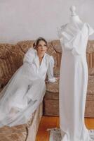 un' donna nel un' bianca vestito si siede su un' divano Il prossimo per un' indossatrice foto