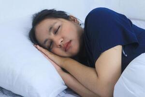 bellissimo asiatico donna dorme comodamente e dolce sogni dire bugie su letto nel accogliente Camera da letto foto