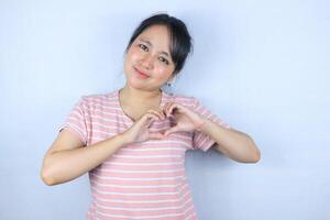 sorridente giovane asiatico donna fabbricazione un' cuore gesto con sua dita nel davanti di sua il petto foto