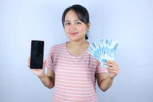 sorridente espressione di asiatico donna Tenere denaro contante rupia e mostrando vuoto mobile schermo. foto