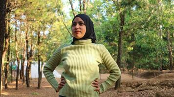 musulmano donna mano su fianchi indossare hijab testa sciarpa nel pino foresta. moderno donna nel estate soleggiato parco foto