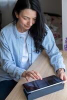 sorridente donna con un' tavoletta su un' tavolo, illustrare un' rilassato approccio per tecnologia nel mezza età, suggerendo equilibrio e digitale fluidità. foto