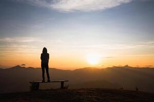 silhouette di un' donna in piedi solo su il superiore di un' montagna e Guardando il Alba. foto