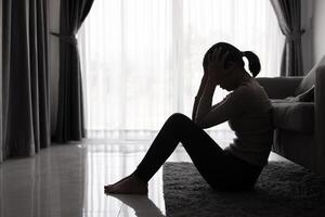 depresso donna, silhouette di adolescente ragazza con depressione seduta solo nel il buio camera. nero e bianca foto. foto