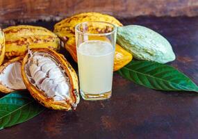 fresco cacao acqua nel bicchiere e metà affettato maturo giallo cacao baccello con bianca cacao seme, cacao succo nel bicchiere su Vintage ▾ di legno sfondo foto