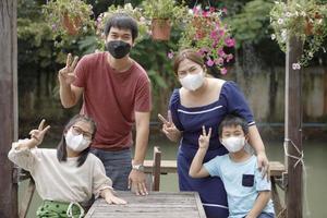 famiglia asiatica che indossa la maschera di protezione per il viso segno a mano vittoria nel parco foto