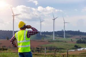 tecnico di ingegneria uomo in piedi partner di chiamata mobile e alla ricerca di turbine eoliche progetto di energia pulita per produrre il servizio di elettricità foto