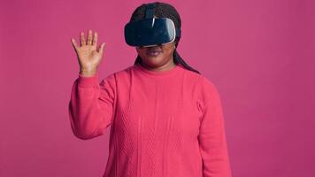 innovativo giovane nero donna gode futuristico simulazione con interattivo dispositivo mentre indossare 3d virtuale la realtà bicchieri nel studio. africano americano di moda fashionista utilizzando moderno vr cuffia. foto