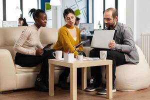 amichevole creativo diverso colleghi squadra discutere di attività commerciale progetto utilizzando il computer portatile e tavoletta a posto di lavoro. multirazziale collaboratori gruppo Lavorando insieme condivisione marketing idee a ufficio incontro foto