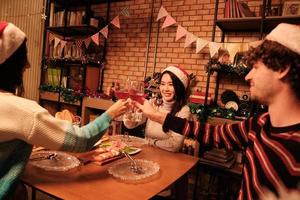 la famiglia e gli amici della felicità stanno festeggiando, alzando i bicchieri e un sorriso allegro con le bevande, si divertono a mangiare cibi nella sala da pranzo di casa, decorati per la festa di Natale e il giorno di capodanno. foto